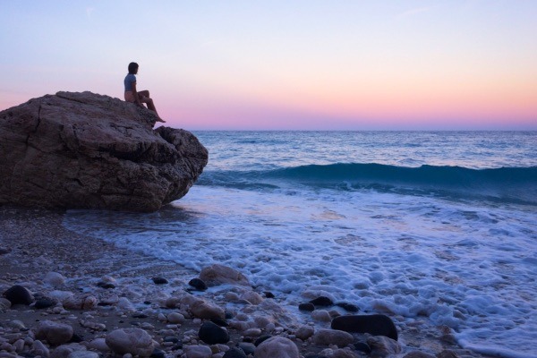 Mädchen sitzt entspannt am Strand auf einen großen Stein und erholt sich